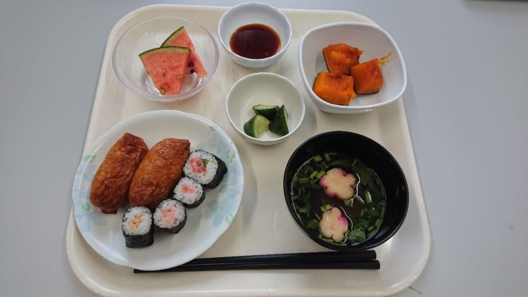 介護施設の食事トレー。揚げ物、寿司、汁物、野菜など栄養バランスの取れた献立。